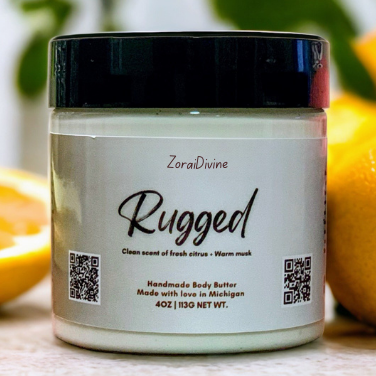 Jar of Rugged handmade body butter on a light surface with oranges in the background