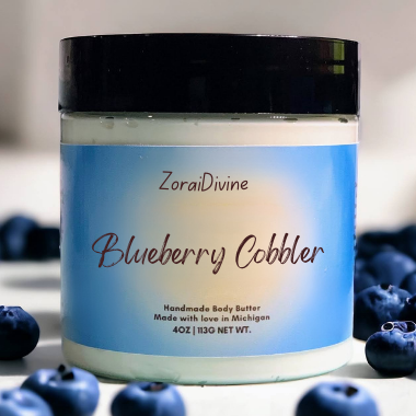 Jar of ZoraiDivine Blueberry Cobbler body butter with blueberries around it.