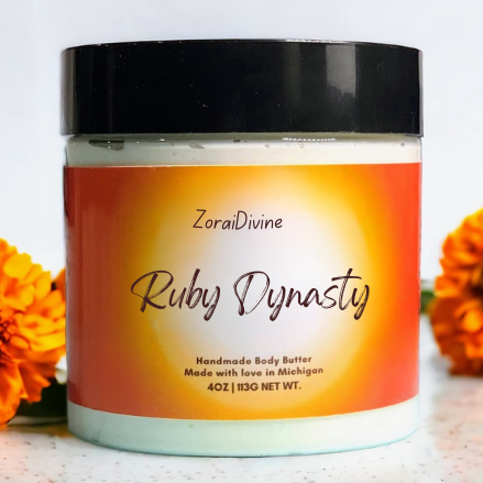 Jar of ZoraiDivine Ruby Dynasty handmade body butter with marigold flowers in the background.