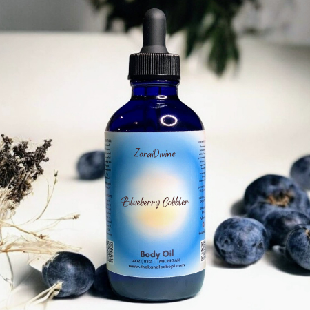Bottle of ZoraiDivine Blueberry Cobbler Body Oil with blueberries in the background.