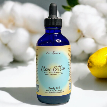 Bottle of ZoraiDivine Clean Cotton Body Oil with a dropper on a white background with flowers and a lemon.