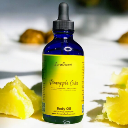 Bottle of ZoraiDivine Pineapple Cake body oil with pineapple slices on a light background