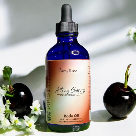 Bottle of ZoraiDivine Astray Cherry body oil with black cherries and flower on a white background