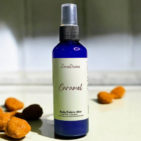 Body mist caramel on a white surface with caramel candy around the bottle.