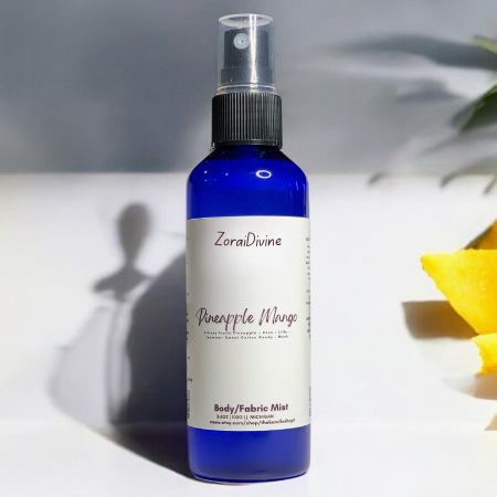 Body mist Pineapple mango on a white counter with mango slices around the bottle.