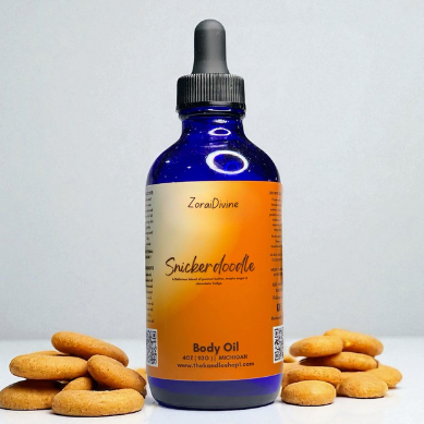Bottle of ZoraiDivine Snickerdoodle body oil with cookies on a light gray background