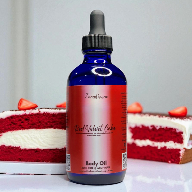 Bottle of ZoraiDivine Red Velvet Cake body oil with a slice of red velvet cake in the background.