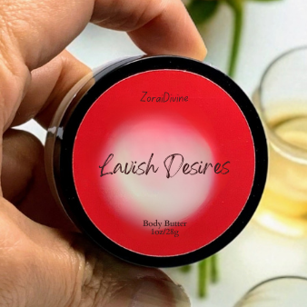 Hand holding a body butter jar labeled 'Lavish Desires' with flowers and a glass in the background