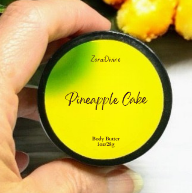 Hand holding a container of 'Pineapple Cake' body butter with a green leaf and yellow fruit in the background.