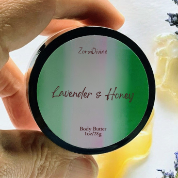 Hand holding a container of 'Lavender & Honey' body butter with lavender flowers in the background.