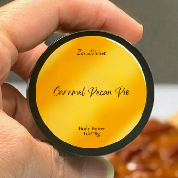 Hand holding a round container of body butter labeled 'Caramel Pecan Pie' with a blurred background