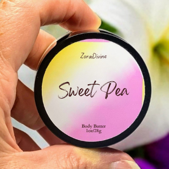 Hand holding a round container labeled 'Sweet Pea' body butter with flowers in the background