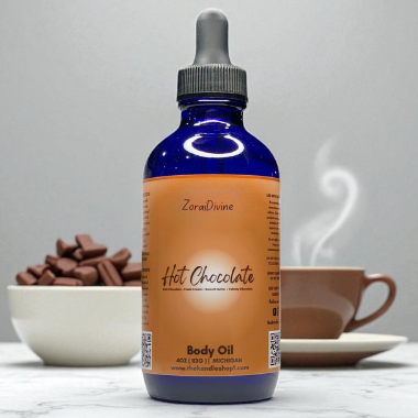 Bottle of hot chocolate body oil with a dropper on a marble surface with a cup of hot chocolate in the background.