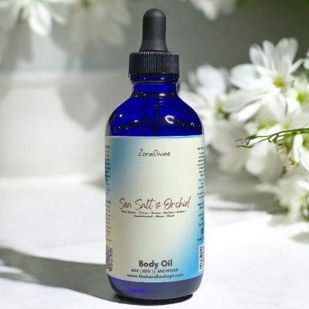 Blue bottle of Sea Salt & Orchid body oil with a dropper on a white surface with flowers in the background