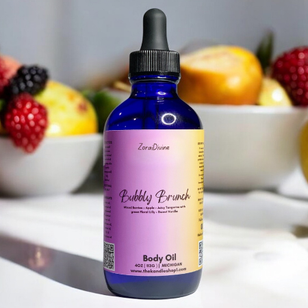 Bottle of 'Bubbly Brunch' body oil with a colorful label, placed on a surface with fruits in the background.