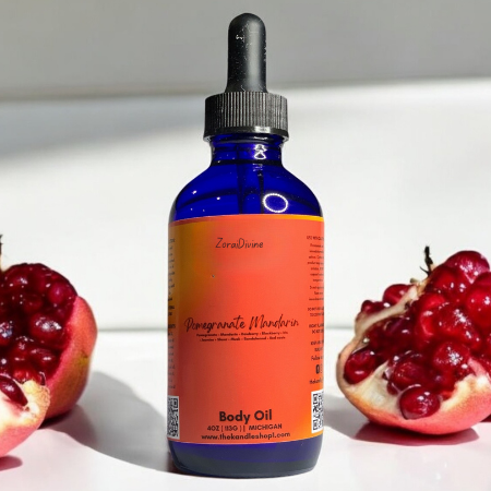 Blue bottle of Pomegranate Mandarin body oil with an orange label between two pomegranate halves on a white surface.