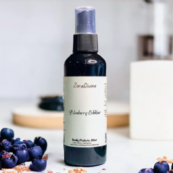 Body mist 'Blueberry Cobbler' with blueberries on a white surface