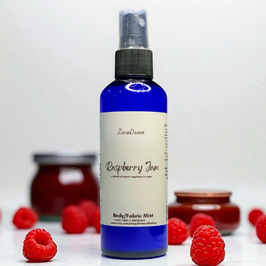 Body mist Raspberry Jam on a white countertop with raspberries on the background.