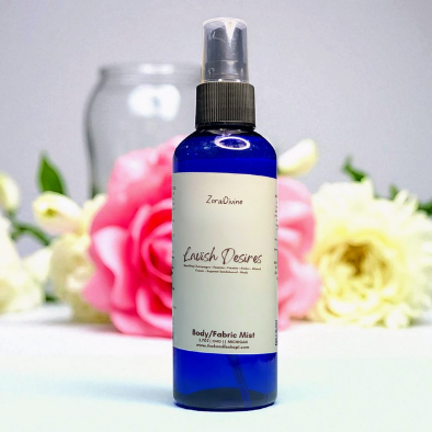 Body mist Lavish Desires on a white countertop with beautiful flowers on the background.