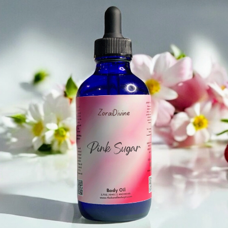 Bottle of ZoraiDivine Pink Sugar body oil with strawberries and flowers in the background