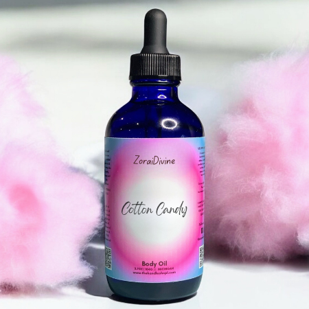 Bottle of ZoraiDivine Cotton Candy Baby Oil with cotton candy in the background
