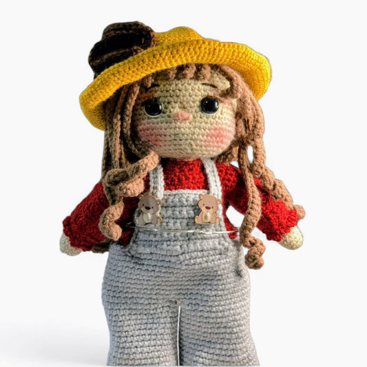 Close-up of an adorable crocheted doll wearing gray overalls and a yellow hat.