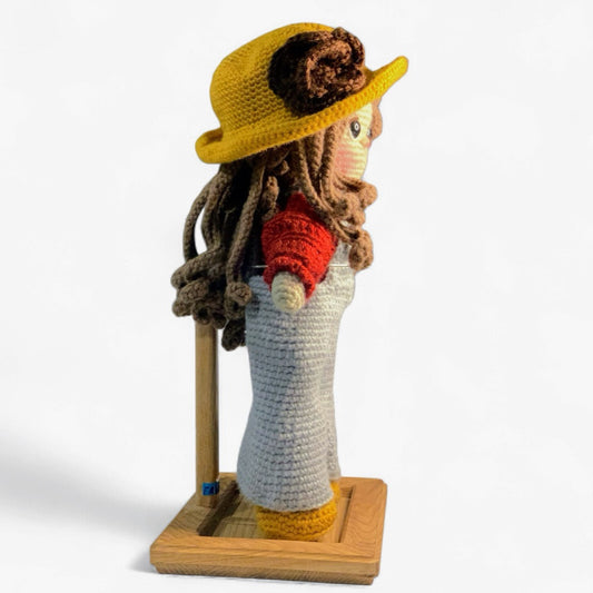 Side view of a handmade crochet doll with long brown hair and a yellow hat.